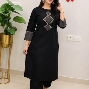 May include: A black knee-length tunic with three-quarter sleeves and matching wide-leg trousers. The tunic features a central diamond-shaped embroidery pattern with red accents and gold detailing, complemented by patterned cuffs on the sleeves.