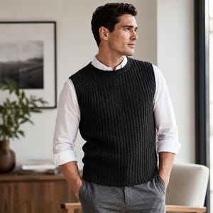May include: A dark charcoal gray sleeveless sweater vest featuring a vertical ribbed knit pattern, worn over a crisp white long-sleeved button-down shirt with the sleeves rolled up, paired with medium gray trousers.