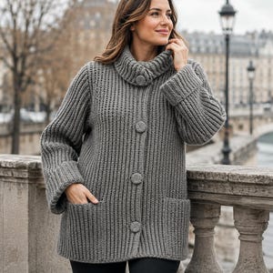 May include: A chunky knit gray cardigan featuring a high collar, long sleeves with wide cuffs, and four large matching buttons down the front. The garment includes two deep patch pockets on the lower front and a thick vertical ribbed texture.