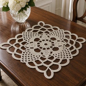 May include: A square, off-white crochet doily featuring a central circular motif surrounded by intricate, repeating geometric patterns and a scalloped, open-work border. The piece is crafted with fine thread, showcasing a detailed, symmetrical design.