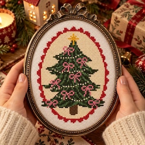 May include: An oval-shaped cross-stitch embroidery featuring a green Christmas tree decorated with small pink bows and a yellow star topper. The design is framed by a red scalloped border on white fabric, all encased in an ornate bronze-colored metal frame.