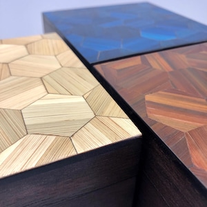 Peut inclure: Trois boîtes rectangulaires dotées de couvercles au motif géométrique hexagonal en mosaïque. Un couvercle est beige clair avec un grain de bois, un est bleu profond avec une finition lisse, et un est brun-rouge chaud avec un grain de bois.
