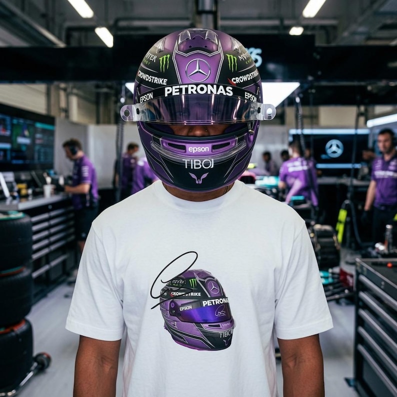 May include: A white t-shirt featuring a graphic of a purple and black racing helmet with the text PETRONAS, EPSON, and TIBOJ. The helmet design includes a Mercedes logo, Monster Energy branding, and a signature graphic above the helmet illustration.