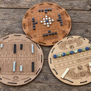 May include: Three circular leather game boards with engraved designs and various game pieces. One board features a grid with black and white cubes, another has a backgammon-style layout with dice, and the third displays Egyptian motifs with colored cubes.