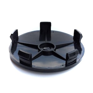 May include: A circular black plastic wheel centre cap featuring a smooth, flat top surface and five evenly spaced mounting clips extending vertically from the underside. The component has a central circular indentation and a star-like structural support.