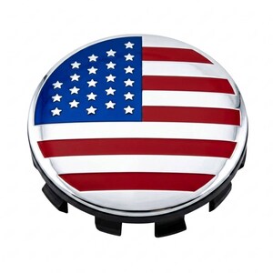 May include: A circular wheel center cap featuring a glossy finish with the American flag design. The emblem displays a blue field with white stars on the left and horizontal red and white stripes on the right, set against a black plastic base.