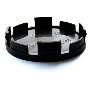 May include: A circular black plastic wheel center cap featuring a metallic silver interior surface. The underside displays molded text including "MADE IN", "ABS", and a date stamp with a circular clock-like indicator showing the number 12.