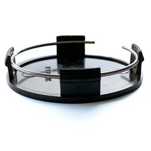 May include: A circular black plastic wheel center cap featuring a metallic silver tension spring wire encircling the inner perimeter. The component includes four evenly spaced black mounting clips extending upward from the flat circular base.
