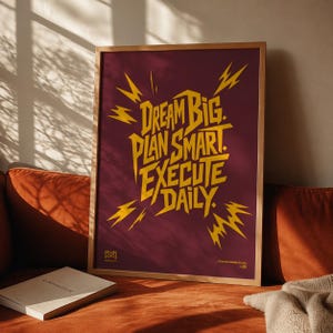 May include: A rectangular framed wall art piece featuring a deep maroon background with bold yellow typography that reads: DREAM BIG. PLAN SMART. EXECUTE DAILY. The text is surrounded by stylized yellow lightning bolt graphics and small logos.