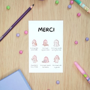 Può includere: Una carta rettangolare bianca con la parola MERCI in nero nella parte superiore, seguita da sei piccole illustrazioni di un personaggio dinosauro rosa in varie pose con didascalie in francese sotto ogni disegno.