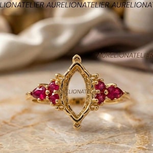May include: A gold ring featuring a central marquise-shaped empty setting flanked by three small, pear-cut red gemstones on each side. The metal band is polished gold, and the design includes delicate metal prongs surrounding the red stones.