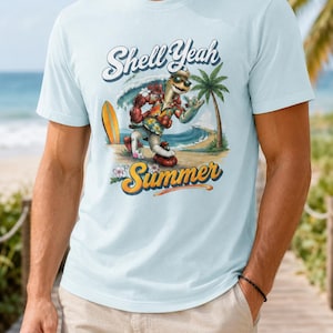 Peut inclure: Un t-shirt bleu clair avec une impression graphique représentant une tortue portant des lunettes de soleil et une chemise à fleurs sur une plage. La tortue fait un geste de la main près d'une planche de surf et d'un palmier. Texte Shell Yeah Summer.