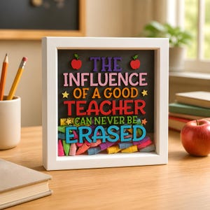 May include: A square white shadow box frame containing a black background with colourful 3D lettering that reads, THE INFLUENCE OF A GOOD TEACHER CAN NEVER BE ERASED. Two red apples and yellow stars accent the text, with colourful pencil erasers below.