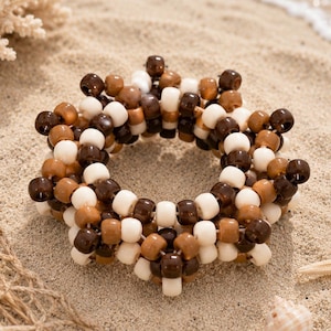 May include: A circular bracelet constructed from interconnected plastic beads in shades of dark brown, light brown, and cream. The beads are arranged in a dense, multi-layered pattern, creating a textured, rounded shape with a hollow center.