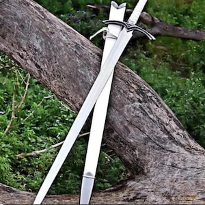 Puede incluir: Una espada de metal plateado con un mango envuelto en blanco y una vaina blanca a juego. La espada presenta una hoja puntiaguda, una guarda con un elemento decorativo central y un pomo. La vaina tiene una punta de metal de color plateado.
