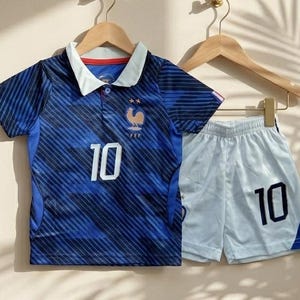 Puede incluir: Una camiseta de f&uacute;tbol azul con cuello blanco, rayas diagonales, el n&uacute;mero 10 y un emblema de gallo con dos estrellas, junto con pantalones cortos de f&uacute;tbol blancos con el n&uacute;mero 10 en azul oscuro y un panel lateral azul en la pierna.