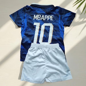 Puede incluir: Una camiseta de manga corta azul y azul oscuro con rayas diagonales, que presenta el nombre MBAPPE y el n&uacute;mero 10 en blanco en la parte posterior, combinada con pantalones cortos deportivos blancos lisos. La camiseta tiene un cuello azul oscuro.