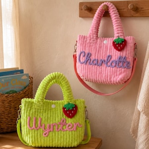 May include: Two corduroy tote bags with top handles and detachable shoulder straps. One bag is pink with the name Charlotte in purple, the other is lime green with the name Wynter in pink. Each bag features a small red strawberry applique.