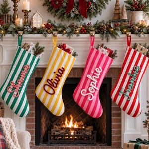 Può includere: Quattro calze di Natale appese a un camino, ognuna con strisce verticali verdi, gialle, rosa e rosse. Ogni calza è personalizzata con un nome in corsivo bianco o rosso: Hanna, Olivia, Sophie e Frankie, con dei regali inseriti all'interno.