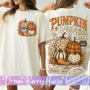 Può includere: Una t-shirt color crema con una piccola grafica di quattro zucche sul petto sinistro e una grande grafica sul retro con il testo PUMPKIN Patch, Farm Fresh & Fabulous, Locally Grown, Fall's Finest Pick, Pumpkins, Corn Maze, Apple Cider.