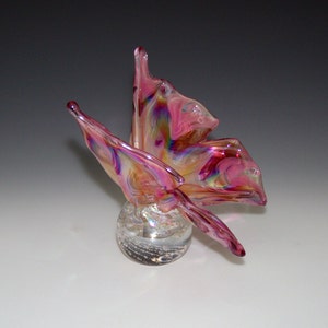 May include: A pink iridescent glass butterfly sculpture with clear glass wings and a clear glass base with air bubbles.