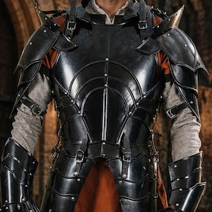 May include: A suit of black metal plate armour featuring shoulder pauldrons, arm bracers, and a chest piece with leather straps. The armour is worn over a beige long-sleeved shirt and a rust-coloured tunic, and the outfit includes a silver metal sword.