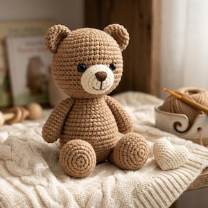 Puede incluir: Un oso de peluche tejido a ganchillo en color marrón con un hocico color crema, ojos oscuros y una nariz bordada. El oso está sentado en posición vertical, con una construcción de hilo texturizado y puntos visibles en cabeza y cuerpo.