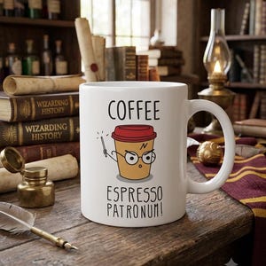 Puede incluir: Una taza de cerámica blanca con una ilustración de un vaso de café con gafas, una cicatriz de rayo y una varita. El texto COFFEE aparece en la parte superior y ESPRESSO PATRONUM! en la parte inferior en letras negras. Tiene un asa lateral.