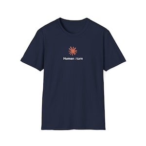 Puede incluir: Una camiseta de manga corta en color azul marino que presenta un pequeño gráfico de estrella en color coral centrado en el pecho. Debajo del gráfico, el texto "Human : turn" está impreso en una fuente blanca sin remates, creando un diseño sencillo.