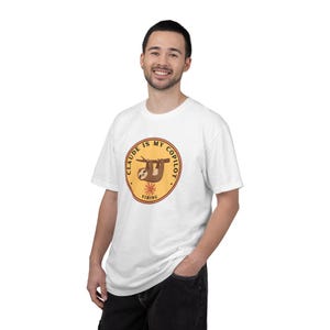 Può includere: Una t-shirt bianca a maniche corte con una grafica circolare sul petto. Il design presenta un bradipo marrone appeso a un ramo con il testo "CLAUDE IS MY COPILOT" e "VIBING" stampato in lettere nere all'interno di un cerchio giallo e arancione.