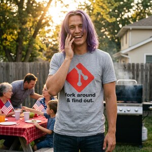 Pode incluir: Uma t-shirt cinzenta mesclada de manga curta com um logótipo Git vermelho em forma de diamante e o texto preto "fork around & find out." estampado na frente. A peça tem gola redonda e um corte padrão, feita de tecido de algodão macio.