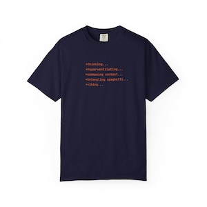 May include: A navy blue short-sleeve t-shirt featuring orange text that reads: *thinking... *hyperventilating... *summoning context... *Untangling spaghetti... *vibing... The shirt has a crew neckline and a standard fit, with a small brand label at the neck.