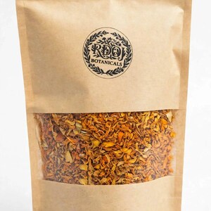Puede incluir: Una bolsa de papel marrón con una ventana transparente que muestra pétalos botánicos secos de color naranja y amarillo. La parte frontal presenta un logotipo circular negro con el texto RDOJ BOTANICALS rodeado por un diseño de corona de hojas.