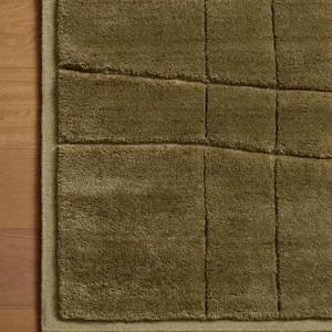 May include: A rectangular area rug in a solid olive green color featuring a tufted, high-pile texture. The surface is divided into a grid of raised, square and rectangular sections created by recessed channels, with a finished bound edge.