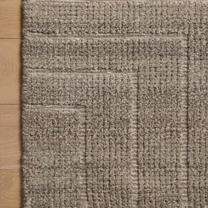 Könnte beinhalten: Ein rechteckiger Teppich mit einer strukturierten, getufteten Oberfläche in einem neutralen Taupe-Farbton. Der Teppich zeigt ein geometrisches Muster aus erhabenen, blockartigen Abschnitten, die in linearen, gitterartigen Formationen angeordnet sind.