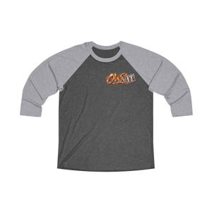 Może przedstawiać: Ciemnoszary t-shirt raglanowy z jasnoszarymi rękawami o długości trzech czwartych i okrągłym dekoltem. Na piersi po lewej stronie znajduje się grafika z napisem "OWN IT" stylizowaną czcionką w kolorach ognistego pomarańczu i żółci.