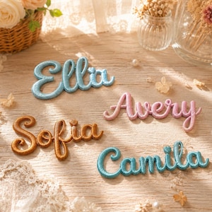 Puede incluir: Cuatro parches bordados con nombres en letra cursiva que muestran los nombres Ella en azul claro, Avery en rosa claro, Sofia en oro metálico y Camila en verde azulado. Cada parche tiene un acabado texturizado en relieve con borde cosido.