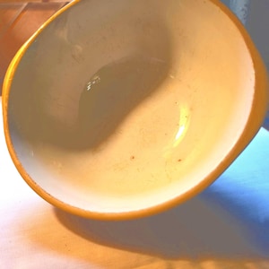 May include: A round ceramic bowl with a smooth, cream-colored interior and a vibrant, solid yellow exterior rim. The bowl features a wide, open basin with a glossy finish, showing subtle signs of use on the inner surface and a clean, curved edge.
