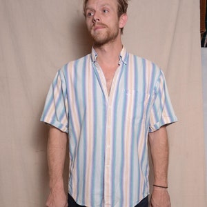 Peut inclure: Une personne portant une chemise à manches courtes boutonnée à rayures bleu clair, blanc et orange avec un jean bleu foncé et des chaussures en cuir marron.