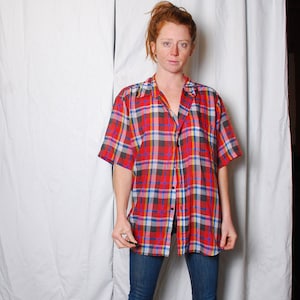 Könnte beinhalten: Eine Person trägt ein rot-schwarzes kariertes Hemd mit blauer Jeans und schwarzen Stiefeln. Die Person steht vor einem weißen Hintergrund.