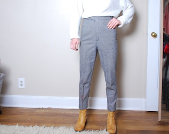 May include: A woman wearing a white sweater and gray high-waisted pants with a subtle pattern. She is wearing brown ankle boots.