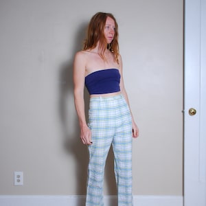 May include: A woman wearing a blue tube top and white pants with a blue and green plaid pattern. She is wearing brown loafers.