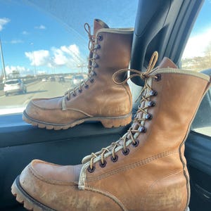 Könnte beinhalten: Ein Paar braune Lederstiefel mit Schnürsenkeln und einer dicken Sohle. Die Stiefel sind abgenutzt und haben einen Vintage-Look.