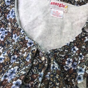 May include: A close-up of a brown and blue floral print top with a white tag that reads "energie" and "100% cotton".