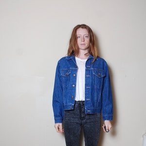 Puede incluir: Una chaqueta vaquera azul con cierre de botones y dos bolsillos delanteros. La chaqueta tiene un estilo cl&aacute;sico y est&aacute; hecha de un material duradero.