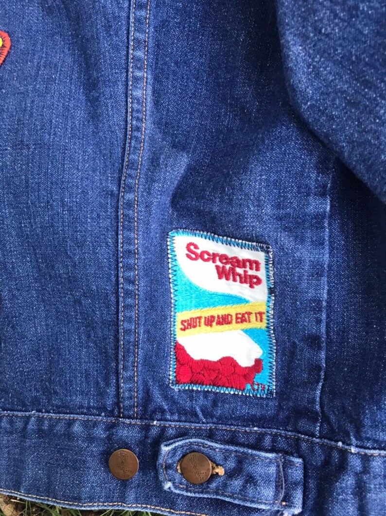 Puede incluir: Chaqueta vaquera azul con un parche bordado en rojo, blanco y azul que dice "Scream Whip" y "Shut Up and Eat It".