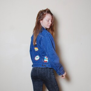 Puede incluir: Una mujer con una chaqueta vaquera azul con parches coloridos en la espalda y pantalones vaqueros de lavado oscuro.