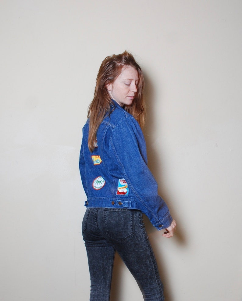 Puede incluir: Una mujer con una chaqueta vaquera azul con parches coloridos en la espalda y pantalones vaqueros de lavado oscuro.