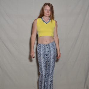 May include: A yellow sleeveless crop top with a V-neck and a gray and white trim, paired with high-waisted, flared pants featuring a gray snakeskin pattern. The outfit is completed with brown shoes.