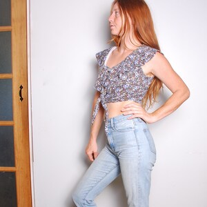 May include: A woman wearing a blue and white floral print crop top with a ruffled neckline and light blue jeans.